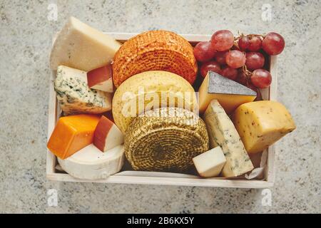 Frais et délicieux différents types de fromages placés dans des caisses en bois avec des raisins