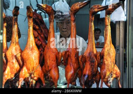 09.01.2014, Yangon, République de l'Union du Myanmar, Asie - un homme se tient derrière des canards rôtis accrochés aux crochets à l'intérieur d'un restaurant. Banque D'Images