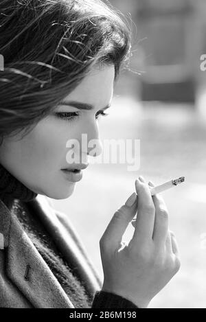 belle élégante triste stressante jeune femme en chandail et manteau fumer la cigarette près de la rivière Banque D'Images