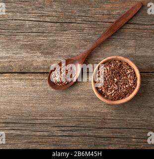 graines de lin brun sec dans une cuillère en bois brun sur une table en bois gris à partir de vieux planches, vue de dessus Banque D'Images