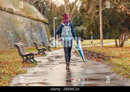 Jeune femme avec parasol arc-en-ciel marchant en plein air dans le parc à un jour de pluie Banque D'Images