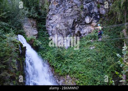 Femme traversant le pont suspendu en direction de la cascade Talbach, sur une route via ferrata dans la vallée de Zillertal, Autriche. Banque D'Images