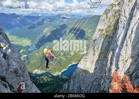 Femme sur l'échelle via ferrata au-dessus du lac Gosau, sur la route Intersport Klettersteig Donnerkogel, en Autriche. Vue sur le grand angle le jour de l'été. Banque D'Images