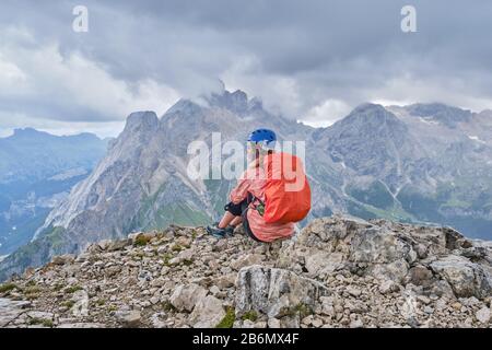 Femme sur Colac Peak, au bout de la via ferrata dei Finanzieri, avec casque sur et sac à dos avec couverture de pluie, bénéficie de la vue panoramique, avec tempête c Banque D'Images