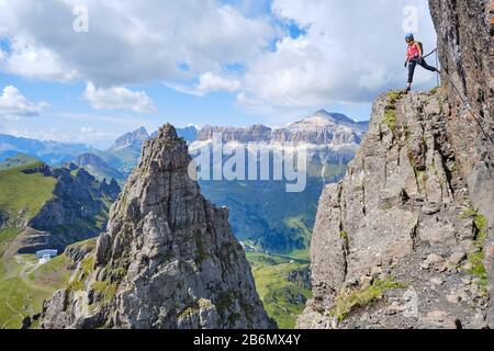 Femme sur via ferrata Delle Trincee (sens Chemin des tranchées), haut au-dessus de pic impressionnant de roche pointue, avec le groupe Sella dans la distance comme backgrou Banque D'Images