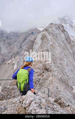 Femme sur via ferrata Eterna Brigata Cadore, montant le sommet est de la ligne de crête de Marmolada (Punta Serauta), avec de faibles nuages et brouillard. Été Banque D'Images