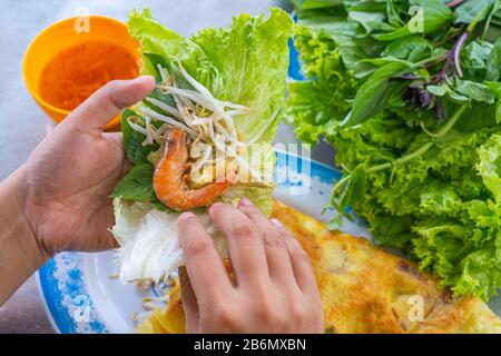 Les gens mangeant Banh Xeo enveloppé de laitue - cuisine vietnamienne Banque D'Images