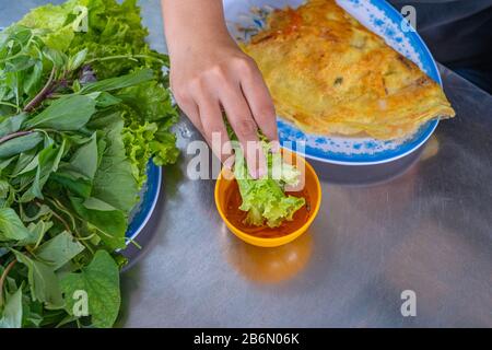 Les gens mangeant la crêpe Banh Xeo avec des légumes et sauce trempée Banque D'Images