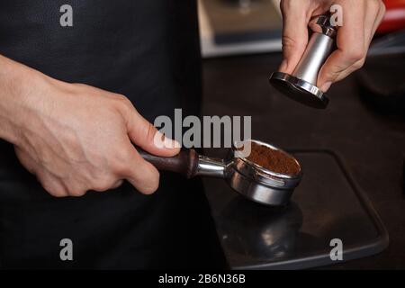 Jeune barista masculin pressant le café moulu dans le porte-filtre sans fond à l'aide d'une autosurveillance. Préparation de l'espresso dans une machine à café professionnelle. Préparation Du Café Banque D'Images