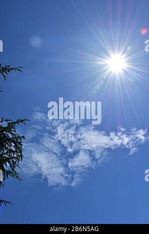 Sun à zenith à midi dans le ciel bleu avec de petits nuages Banque D'Images