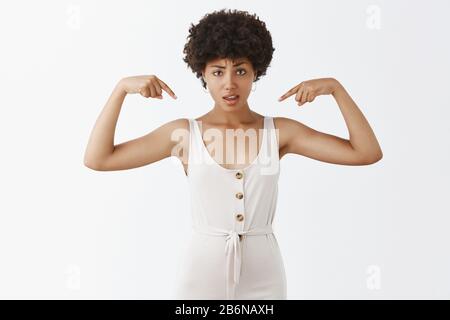 Photo studio d'intense confus et douteux attrayant Afro-américain femme blogueuse dans des combinaisons blanches avec la coiffure d'afro pointant vers épaules Banque D'Images