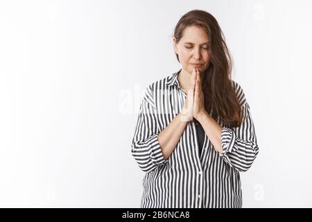 Femme âgée de 50 ans avec de longs cheveux près des yeux Bow tête avec des yeux fermés et sérieuse focalisée expressiong tenant les mains dans prier et supplication, priant Banque D'Images