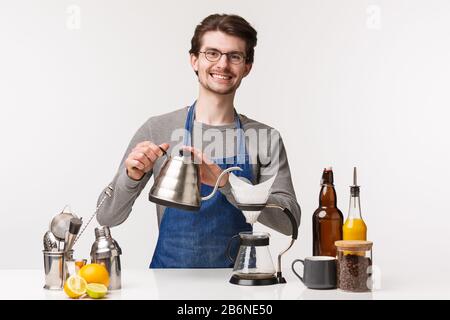 Barista, employé de café et concept de barman. Portrait d'un jeune homme sympathique et gai dans le sourire du tablier au client tout en versant de l'eau Banque D'Images