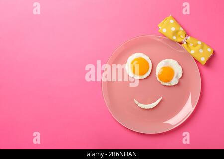 Sourire visage fait de plaque avec des œufs frits sur fond rose, vue de dessus Banque D'Images