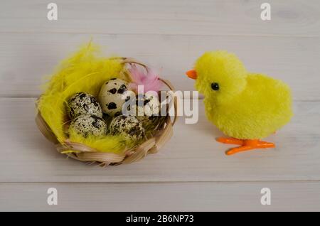 Fond de carte de Pâques. Jouet poulet près d'un nid avec des œufs et des plumes à pois sur un fond blanc en bois. Joyeuses pâques. Vue latérale. Banque D'Images