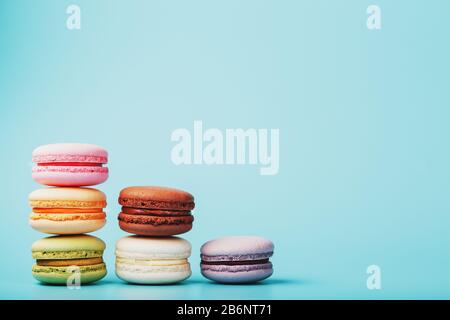 Les cookies macaroni de différentes couleurs sont disposés en forme de marches pyramidales sur un fond bleu. Espace libre. Le concept de minimalisme Banque D'Images