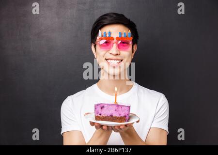 Concept de célébration, de vacances et d'anniversaire. Gros plan portrait de l'homme asiatique excité et heureux et joyeux célébrant le b-day dans des verres drôles, tenant le gâteau Banque D'Images