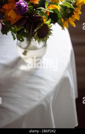 Un bouquet avec des fleurs sauvages rustiques d'été, des tournesols se trouve sur la table avec une nappe blanche. Style de vie. Espace de copie. Film en train de bricoler. Photo Moody. Banque D'Images