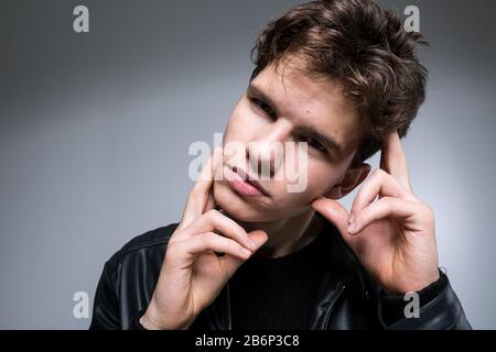 Portrait grand angle jeune homme modèle en vêtements noirs posant en studio fond blanc. Guy porte une veste en cuir classique noir. Beau jeune Banque D'Images