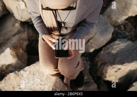 Gros plan photo des mains féminines tenant le téléphone mobile et prenant des photos de lac sur un jour nuageux. Elle envoie des SMS sur son smartphone et prend son selfie. Banque D'Images