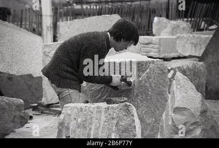 1970, historique, un jeune sculpteur masculin travaillant sur de grandes roches de pierre, à la South Bank, Londres, Angleterre, Banque D'Images