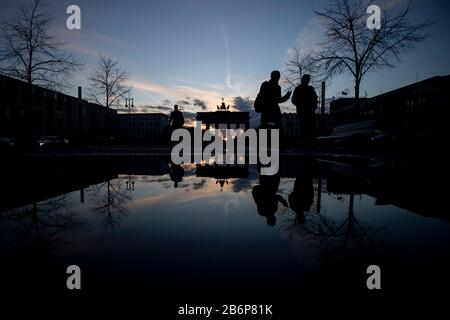 Berlin, Allemagne. 11 mars 2020. Passants à pied sur Pariser Platz au crépuscule devant la porte de Brandebourg. Le paysage se reflète dans une flaque. Crédit: Christoph Soeder/Dpa/Alay Live News Banque D'Images