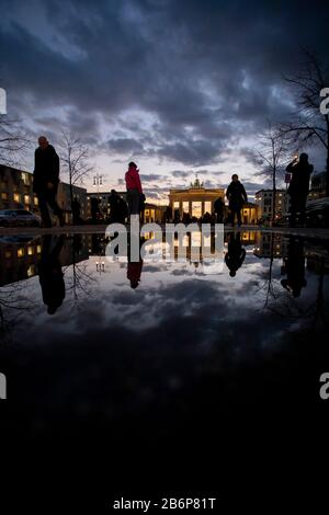 Berlin, Allemagne. 11 mars 2020. Passants à pied sur Pariser Platz au crépuscule devant la porte de Brandebourg. Le paysage se reflète dans une flaque. Crédit: Christoph Soeder/Dpa/Alay Live News Banque D'Images