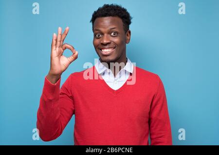 Jeune afro-américain ayant un regard heureux, souriant, gesturant, montrant OK signe approuver votre choix. Concept de langage corporel Banque D'Images