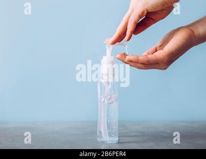 Vue rapprochée de la femme à l'aide d'un distributeur de désinfectant pour les mains, fond bleu propre minimaliste. Concept de santé. Banque D'Images