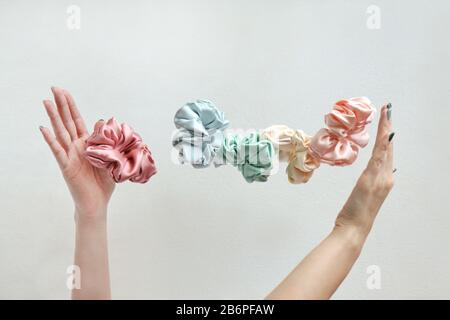 Beaucoup de flotter En soie Colorée Scrochies sur les femmes mains isolées blanc. Outils et accessoires de coiffure. Cheveux Scrochies, bandes élastiques, vol Banque D'Images