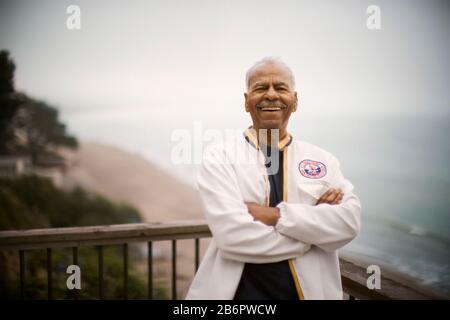 Portrait d'un homme adulte souriant debout avec des bras repliés sur une terrasse donnant sur l'océan. Banque D'Images