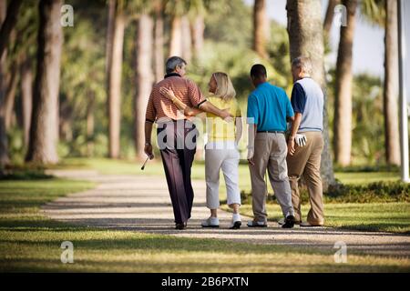 Mid-adult mari et femme marchant avec deux amis masculins adultes sur un parcours de golf. Banque D'Images