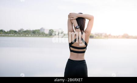 Une jeune femme asiatique qui s'étire avant et après une séance de conditionnement physique à côté du lac dans le parc. Une belle femme dans des vêtements de sport qui s'étirent en plein air Banque D'Images