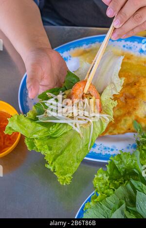 Les gens qui utilisent des baguettes et enveloppent la crêpe Banh Xeo avec de la laitue Banque D'Images