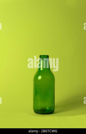 Petite bouteille en verre vert vide sans couvercle et étiquette sur fond vert vif. Peut être utilisé comme maquette pour le jus ou la bière. Banque D'Images