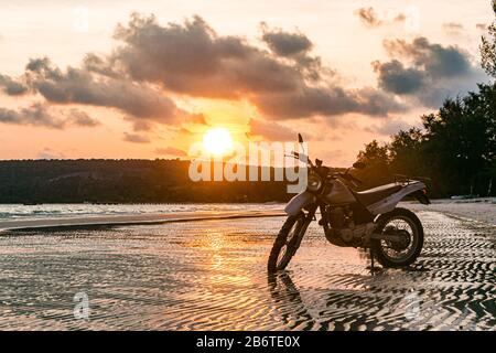 Une moto argentée se trouve sur la plage au coucher du soleil Banque D'Images