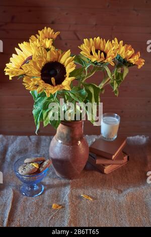 Bouquet de tournesols gaies dans un pichet en céramique , à côté d'un verre de lait, de biscuits et de livres. Banque D'Images