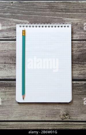 Le Bloc-notes avec une feuille blanche vierge dans un papier de vérificateur avec un simple crayon de graphite se trouve sur le fond de panneaux en bois Banque D'Images