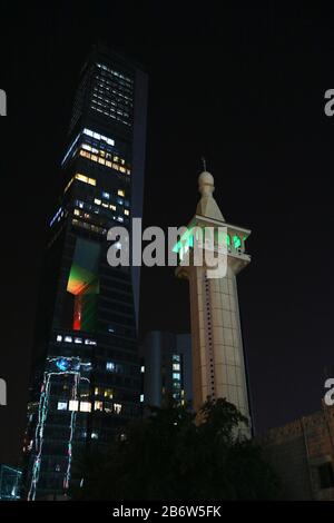 Photo nocturne du minaret éclairé de la mosquée éclipsé par le gratte-ciel moderne avec des lumières Banque D'Images