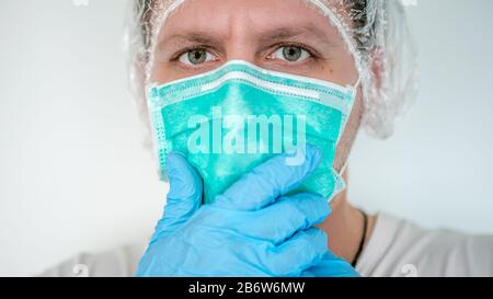 Mains avec gants bleus portant un masque médical pour protéger les voies respiratoires supérieures. La main de l'homme met sur un masque facial de protection contre le virus Banque D'Images