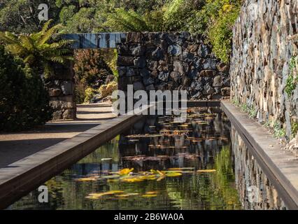 Étang de jardin, mur de pierre, chemin de la porte de voûte entourée d'arbres Banque D'Images