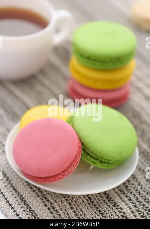 Gros plan de macarons colorés sur la plaque blanche et une tasse de thé Banque D'Images