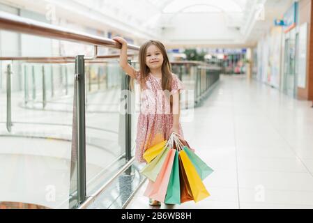 Jolie petite fille souriante avec des sacs à provisions se posant dans la boutique. Des moments agréables de petite princesse, un enfant sympathique qui s'amuse à l'appareil photo. Banque D'Images