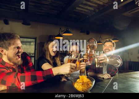 Les amateurs de sport applaudisent au bar, au pub. Prendre des verres à bière tout en regardant le championnat, la compétition. Groupe multiethnique d'amis enthousiasmés par la traduction. Émotions humaines, expression, concept de soutien. Banque D'Images