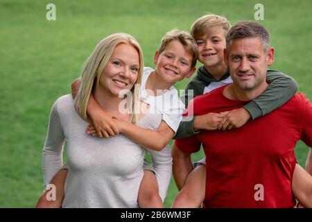 Une vue de face d'une belle famille jouant ensemble dans la cour arrière, les parents peuvent être vus donnant à leurs enfants des porgybacks. Banque D'Images