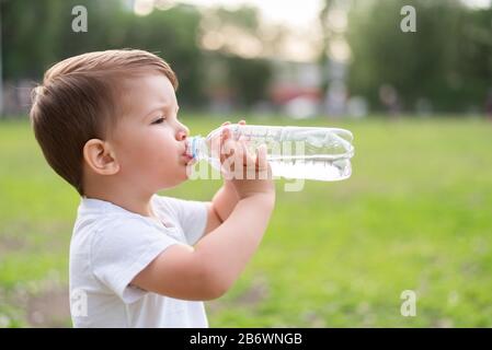 Beau bébé boit de l'eau propre à partir d'une bouteille sur une journée ensoleillée dans la nature Banque D'Images