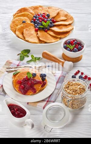 gros plan de crêpes au gruau servies avec des bleuets frais et des canneberges sur une plaque blanche avec sauce aux canneberges, vue verticale d'en haut Banque D'Images