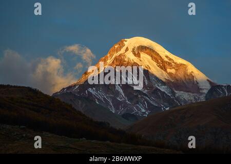 Haut Sunlighted du support couvert de neige sur fond bleu ciel. Scène du lever du soleil. Le mont Kazbek est l'une des principales montagnes du Caucase située à i Banque D'Images