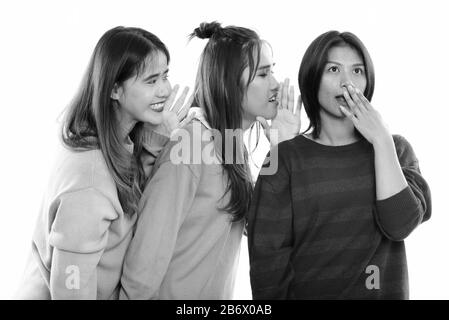 Studio shot of young Asian woman looking choqué avec les deux amis de murmurer d'un côté Banque D'Images