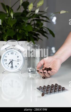 Réveil blanc et pilules médicales avec un verre d'eau sur la table. Santé et médecine. Vitamines et compléments minéraux en capsules. Banque D'Images